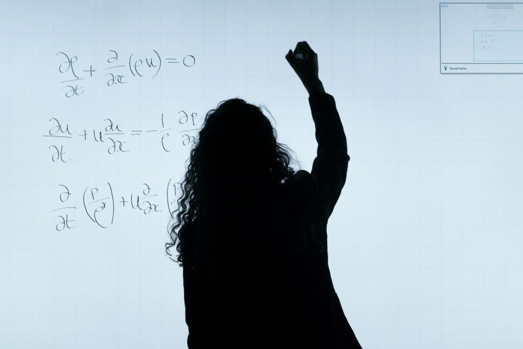 Silhouette of a person writing equations on a large whiteboard