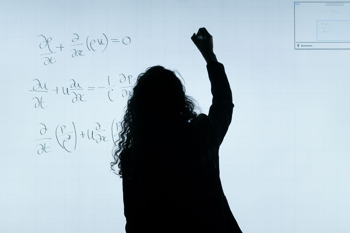 Silhouette of a person writing equations on a large whiteboard
